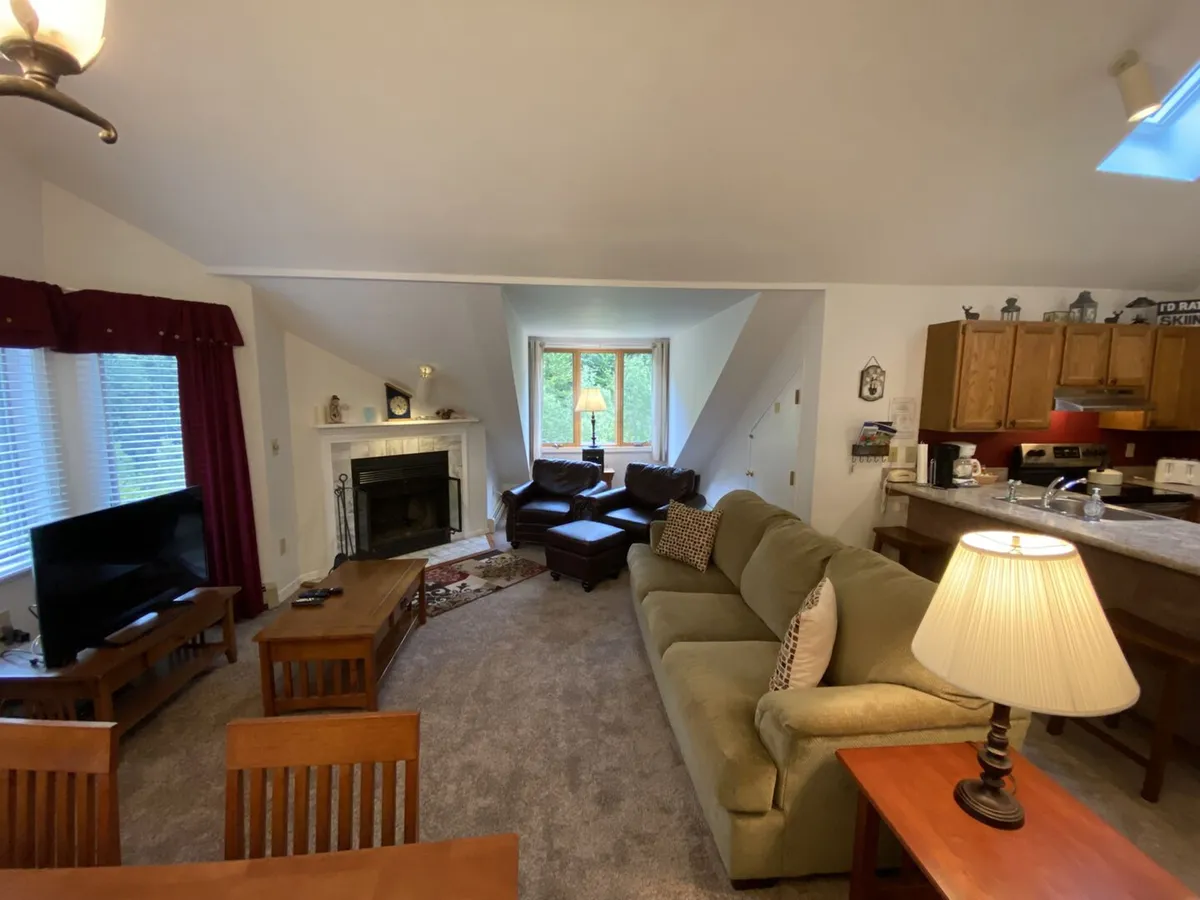 This interior image features a cozy living area with a marble wood-burning fireplace, plush sofa, and large windows that invite natural light, complemented by a dining table and coffee table for gathering. The scene suggests warmth, relaxation, and opportunities for socializing after a day of exploration.