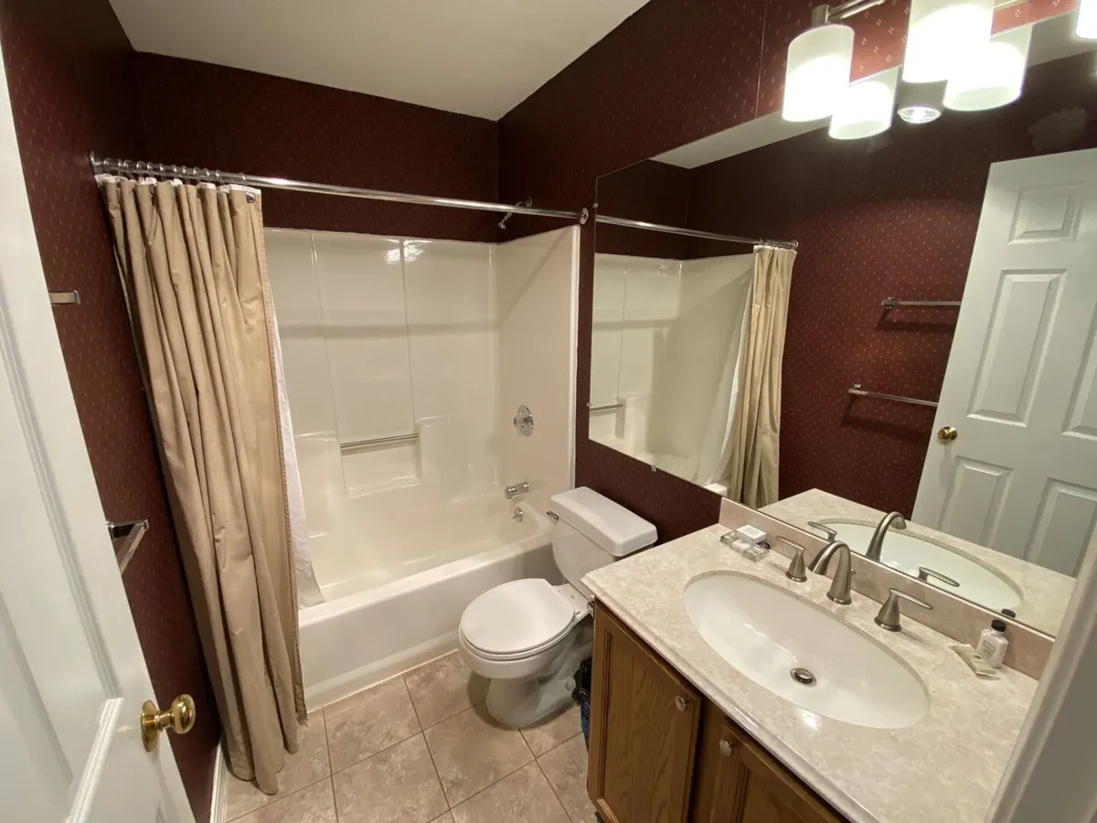 A clean, modern bathroom featuring a full-size bathtub, double sinks with mirrors, practical light fixtures, and a toilet. The space feels bright and functional—ideal for morning routines or relaxing baths after outdoor activities.