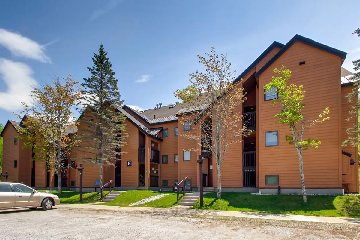 This image showcases the wooden exterior of the condo at Pico Village Resort, with a landscaped front yard, steps leading to the entrance, and a welcoming parking area. The scene gives a sense of warmth and approachability, inviting families to experience easy access to mountain activities right from their doorstep.