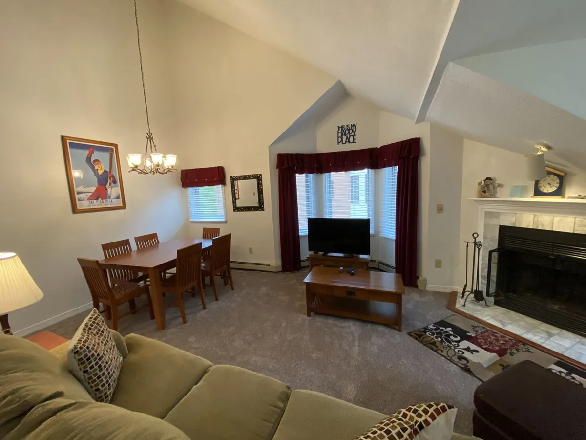 A welcoming living area combining a dining table, sofa, fireplace, television, and decorative artwork. The setup is inviting for family gatherings, movie nights, or intimate dinners, capturing the multi-functional atmosphere of the main living space.